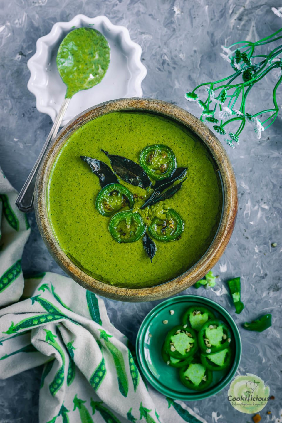 Mint Cilantro Chutney in a round bowl with sliced jalapenos on the side and a kitchen towel next to it