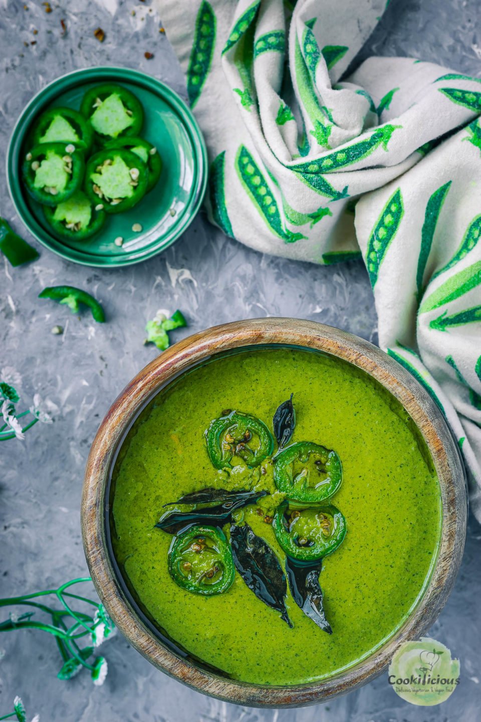 a bowl of Mint Cilantro Chutney with a small plate filled with sliced jalapenos on the side along with a kitchen towel