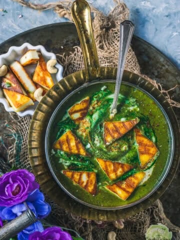 Restaurant Style Palak Paneer in a round platter with a spoon in it and some grilled paneer on the side