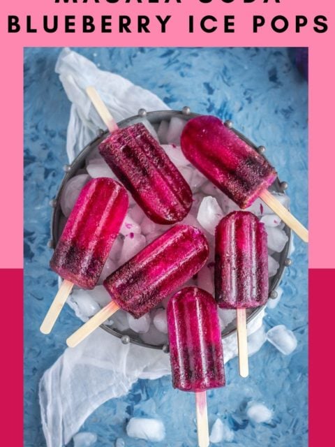 many Masala Soda Blueberry Popsicles placed on a tray filled with ice cubes with text at the top