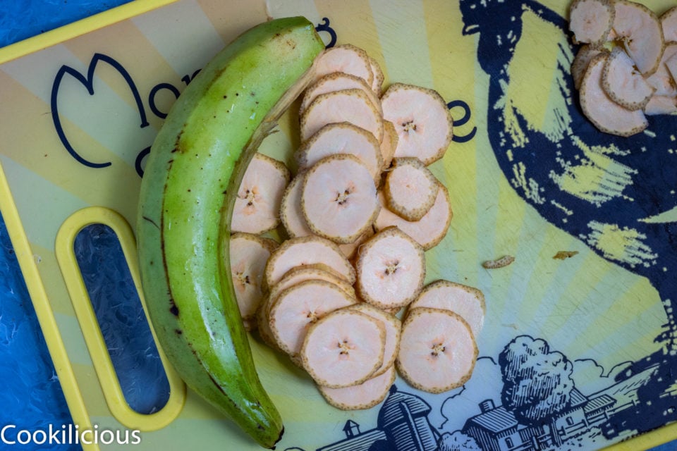 a raw banana placed next to slices of another raw banana used to make Fried Raw Banana Vegan Chips