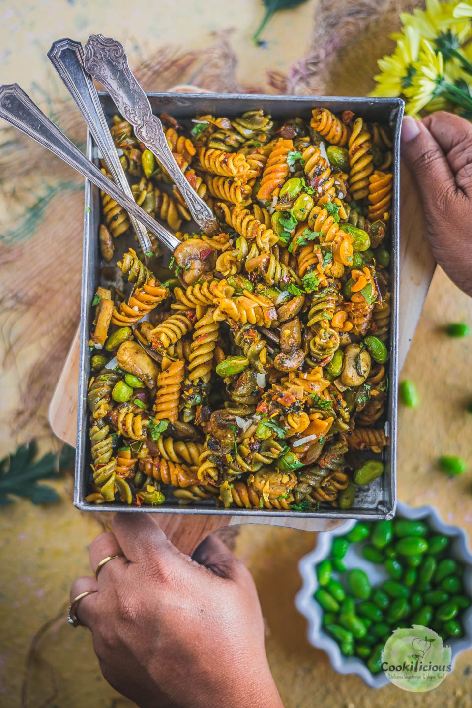 a pair of hands holding a wooden platter which holds a serving tray filled with Indian Pasta Recipe | One-Pot Vegan Curry Pasta Dish