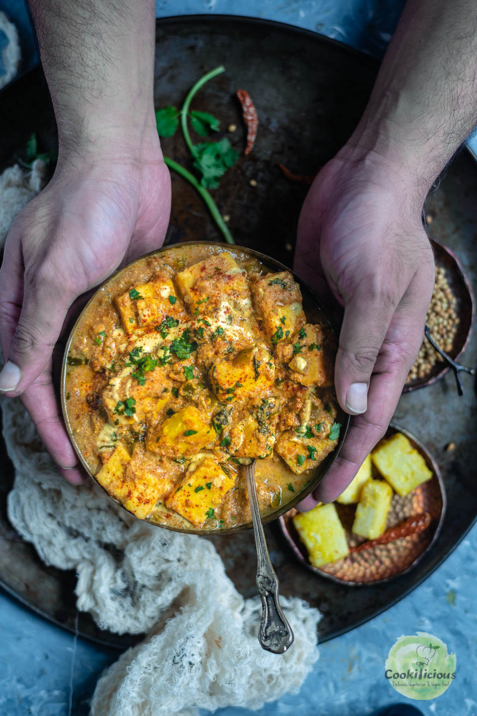 a set of hands holding a bowl of Fried Paneer Butter Masala