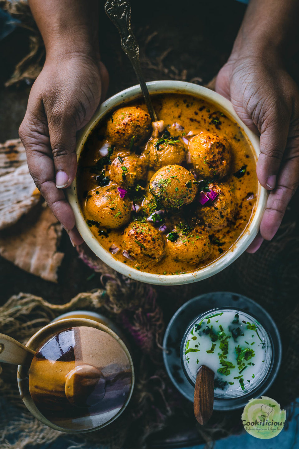 a set of hands holding a bowl of Dum Aloo