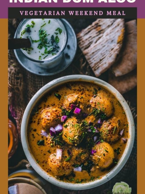 Dum Aloo in a round serving bowl with a glass of buttermilk on the side and text at the top