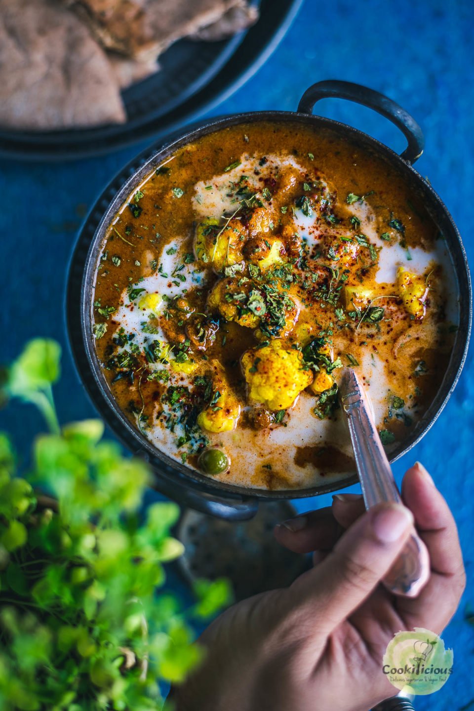 a hand putting a spoon into a small kadai of Cauliflower Tikka Masala - Easy Vegan Curry