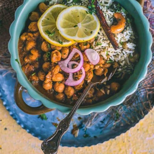 a bowl of Vegan Chana Masala served with jeera rice and lemon slices on top