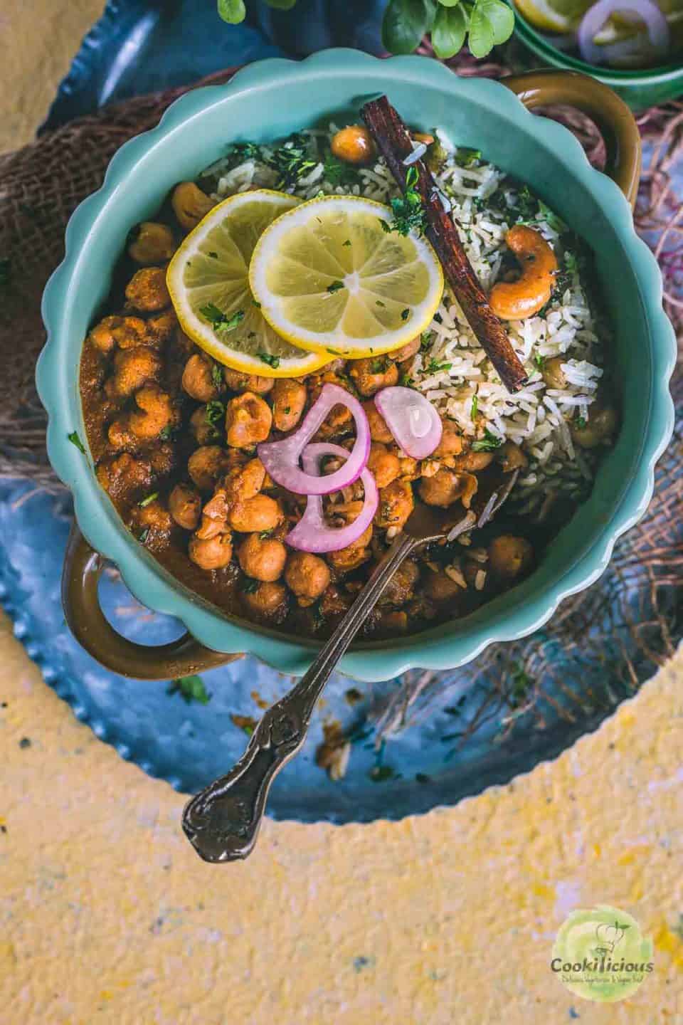 a bowl of Vegan Chana Masala served with jeera rice and lemon slices on top