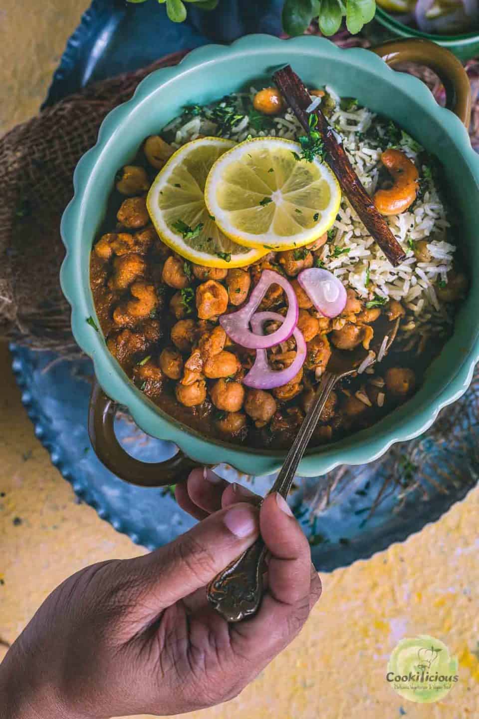 a hand holding a spoon and digging into a bowl of Vegan Chana Masala