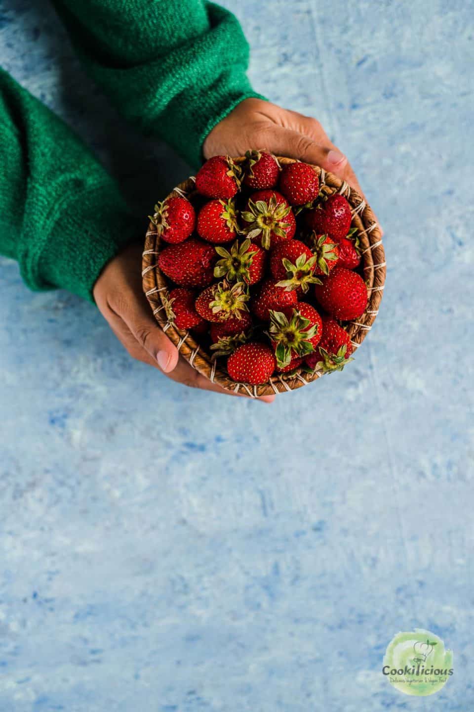 a set of hands holding a small basket filled with strawberries