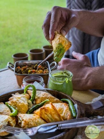 a man sitting at the dining table and dunking a Vegetable Puff Pastry Samosa into a bowl of green chutney