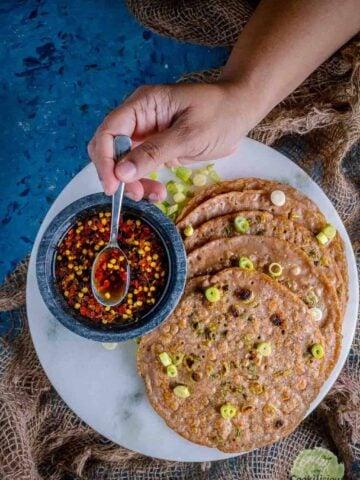 Chinese Scallion Pancakes served in a platter with one hand putting a spoon into the dipping sauce next to it