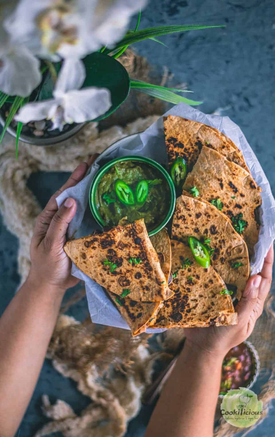 a set of hands holding a platter filled with Tandoori Cheese Quesadilla.