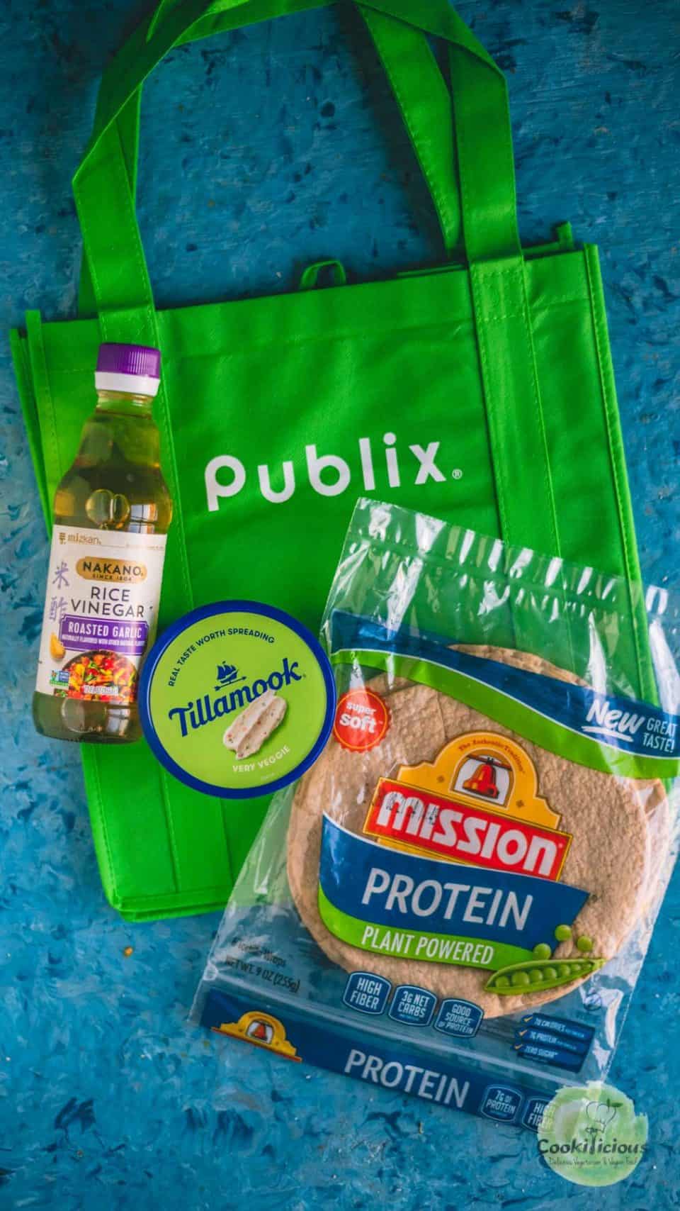 a Publix shopping bag with a packet of tortillas, rice vinegar and cream cheese spread around it