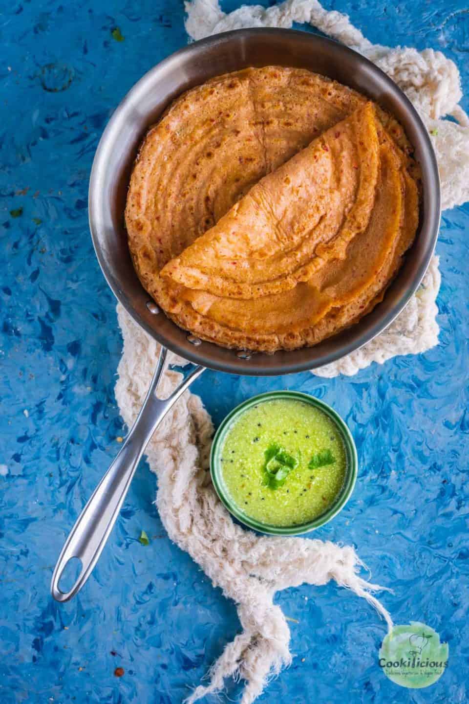 Oats Carrot Dosa in a steel skillet with a bowl of green chutney on the side