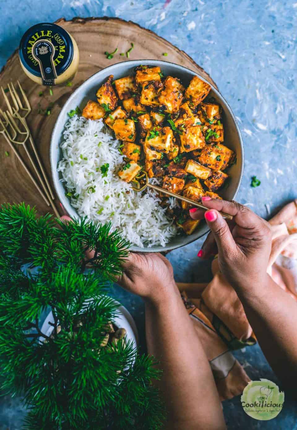 one hand holding the bowl and the other hand digging into the bowl filled with chilli paneer with a fork