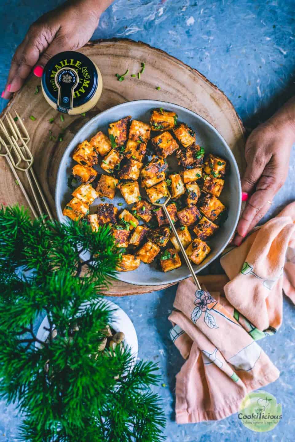 a set of hands serving a platter with a bowl of chilli paneer in it