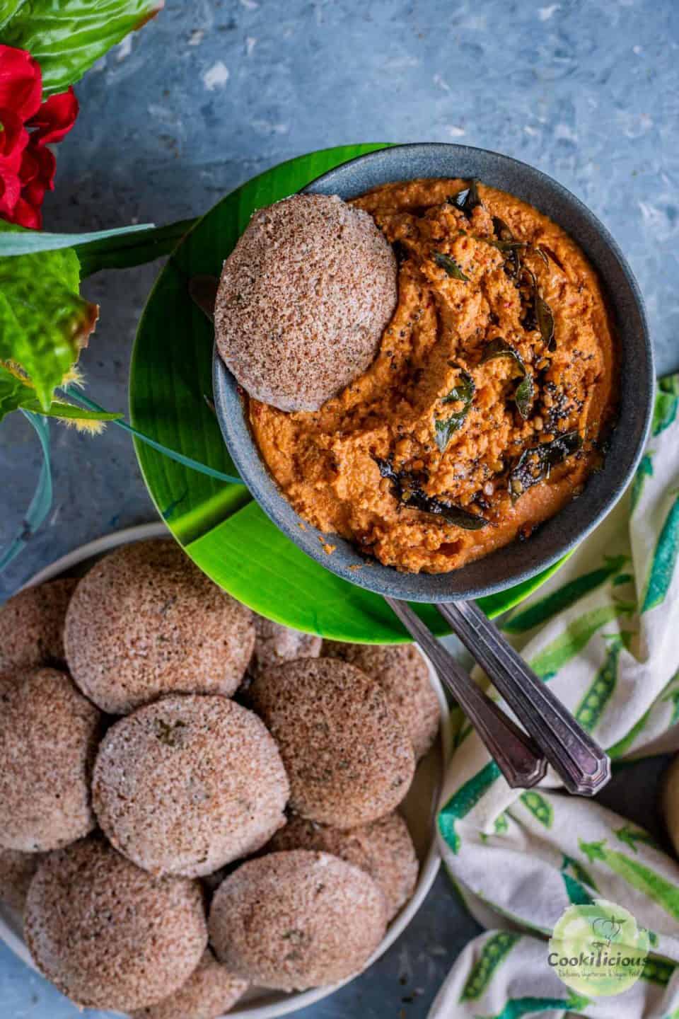 one Teff Idli With Beet Leaves dunked into a bowl of chutney