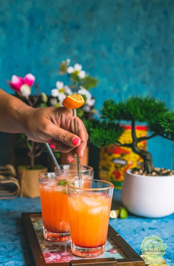 a hand stirring a glass of Rose Lemonade with a stirrer