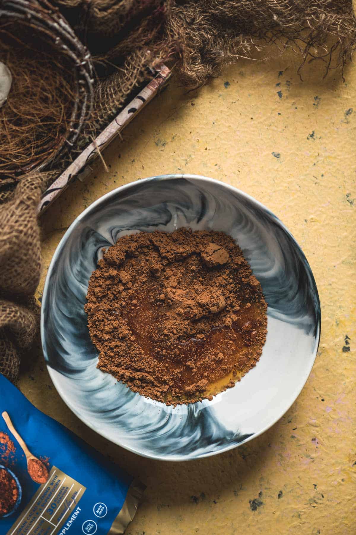 Maple syrup and vanilla extract added to cacao powder in a bowl.