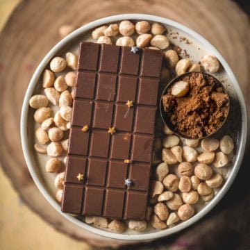Homemade vegan chocolate bar topped with edible stars, plated with macadamia nuts and cacao powder.