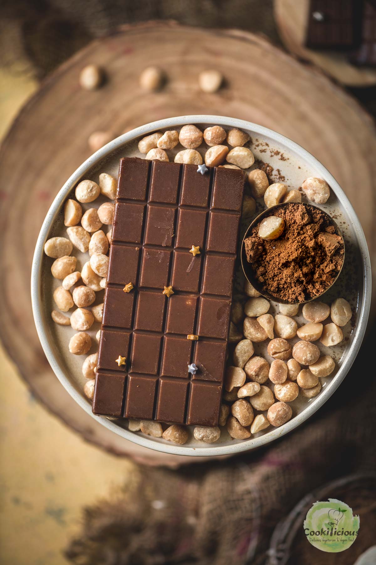 Homemade vegan chocolate bar topped with edible stars, plated with macadamia nuts and cacao powder.