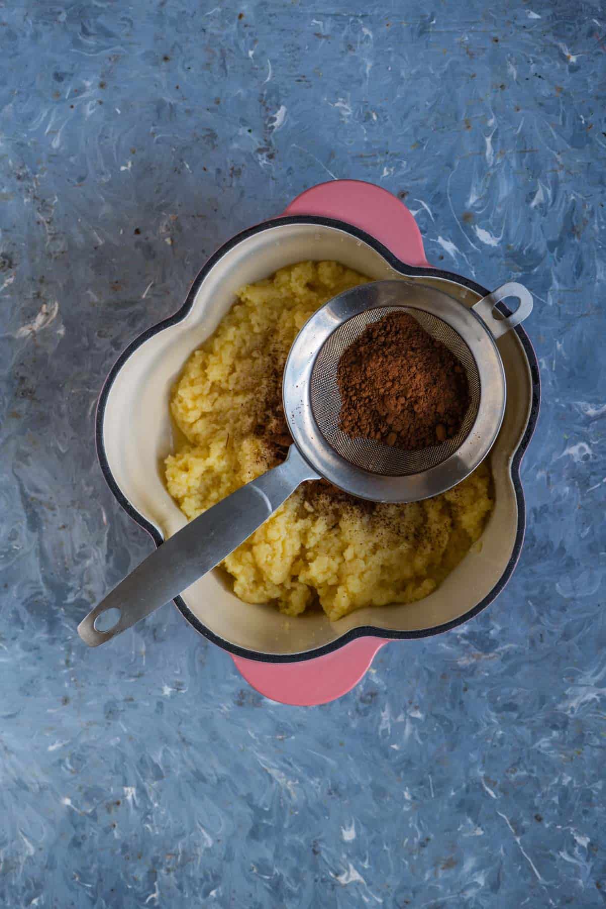 Cocoa powder being sifted into the khoya mixture.