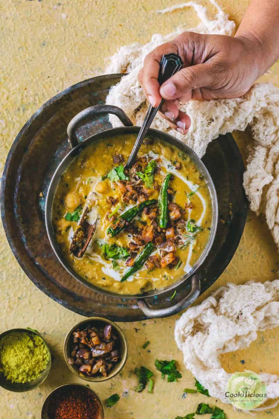 a hand digging a spoon into a bowl of Shahjahani Dal