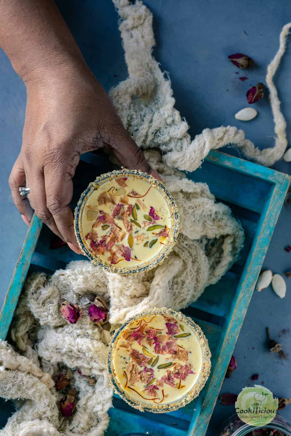 one hand picking up a glass of thandai from a tray