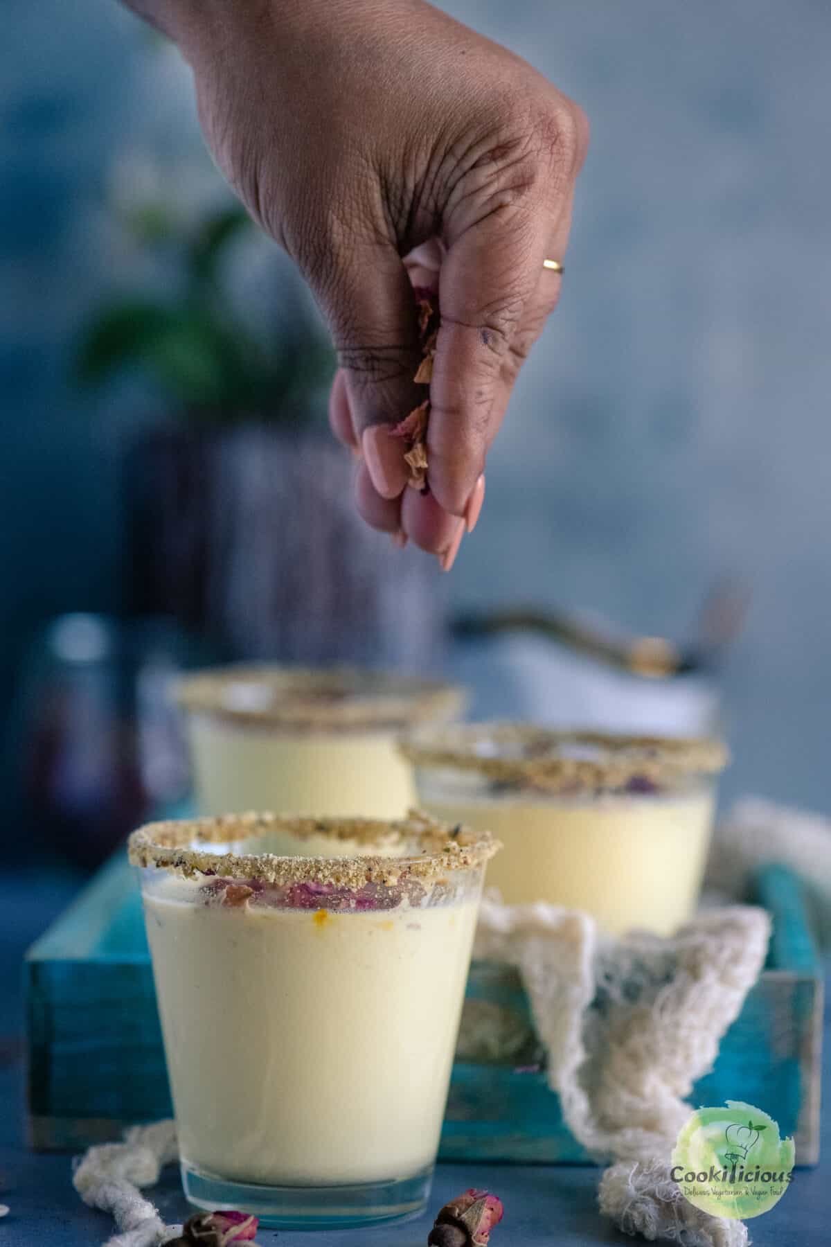 a hand sprinkling rose petals over a glass of thandai drink