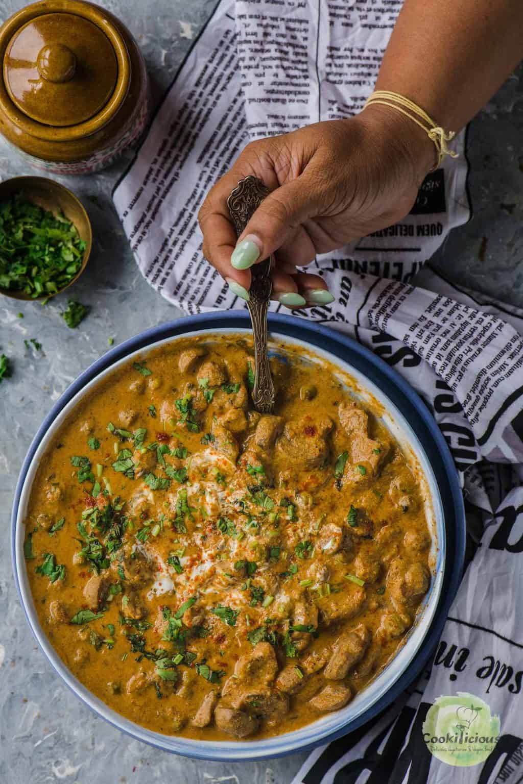 a hand holding a spoon and digging into a bowl of Mushroom Masala