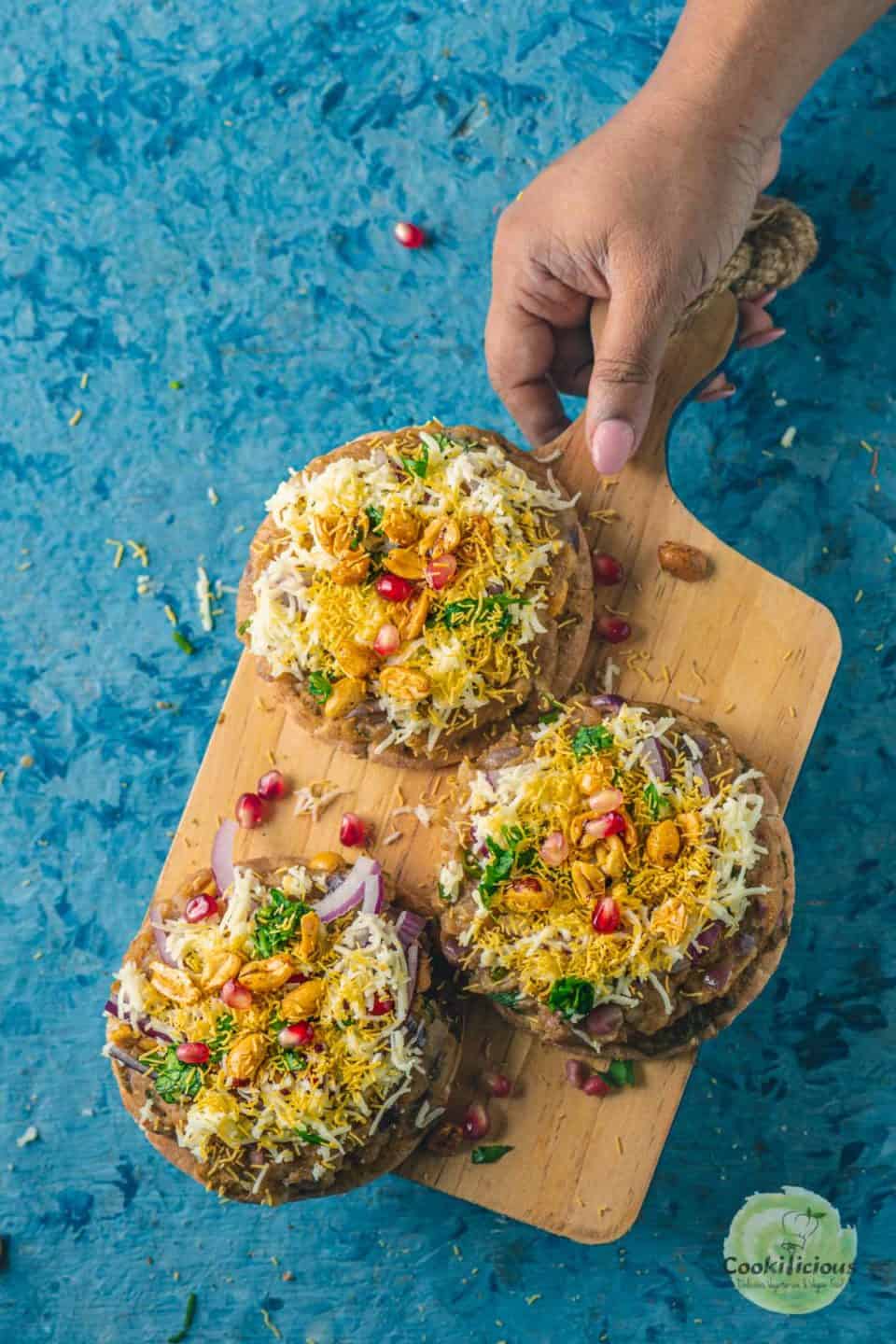 a hand holding a wooden board that has 3 Dabeli Pita Bread Pizzas