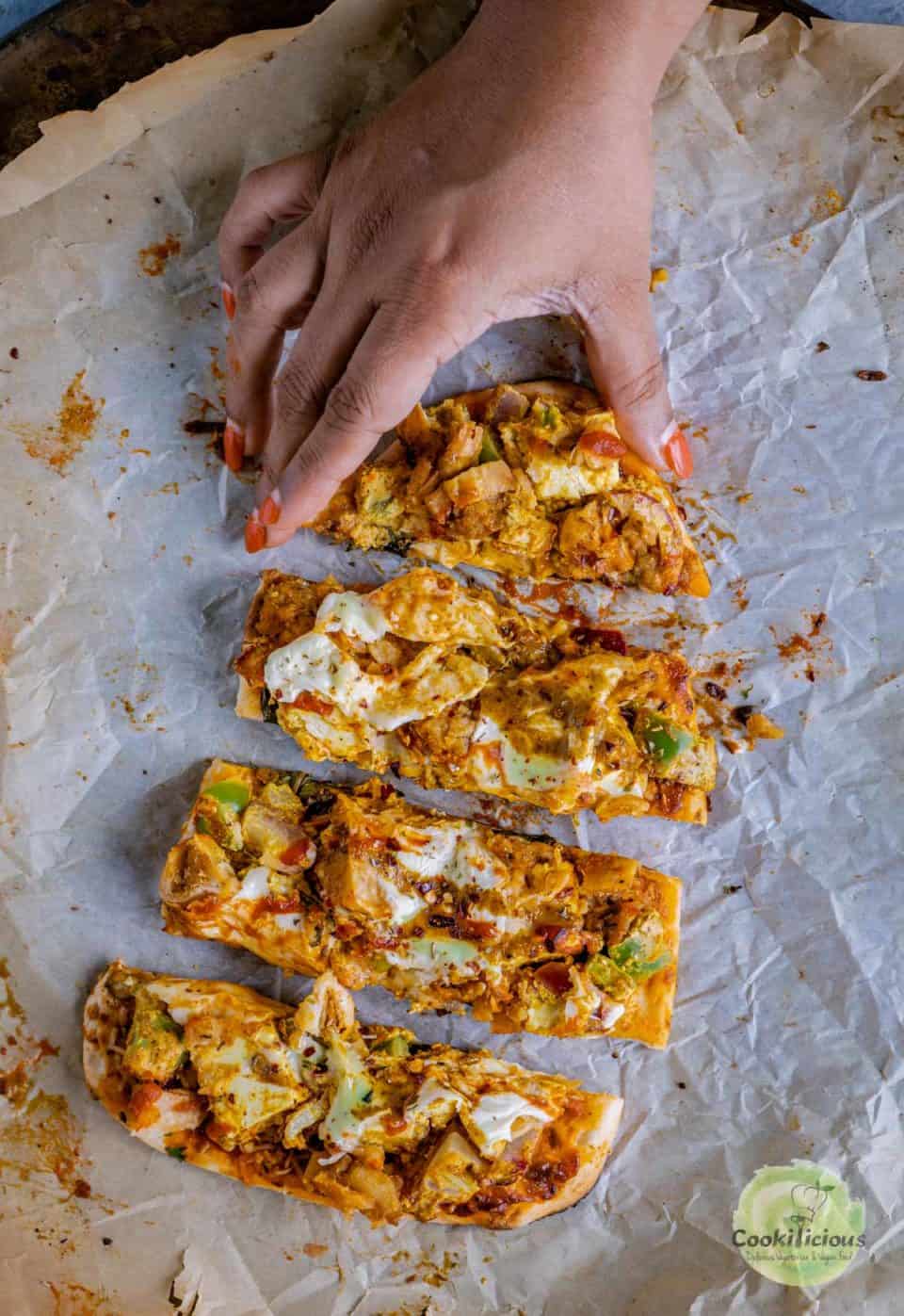 a hand picking up one slice of Paneer Naan Pizza