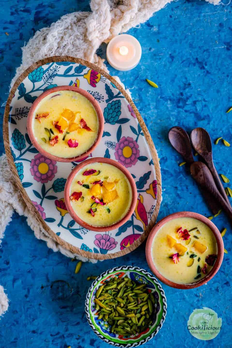 2 bowls of mango phirni in a tray and one bowl next to it