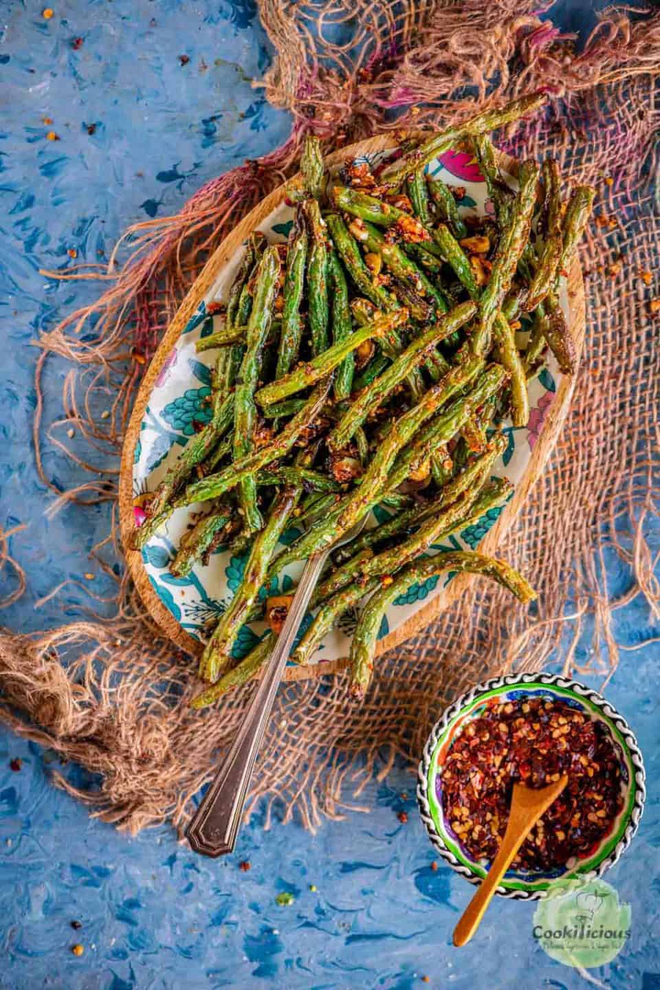 a plate full of Air Fried Green Beans served with a bowl of red pepper flakes on the side