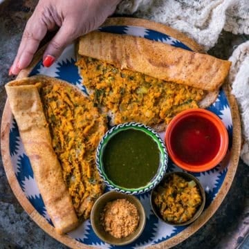 a hand holding a plate filled with 2 Masala Dosa with Sweet Potato