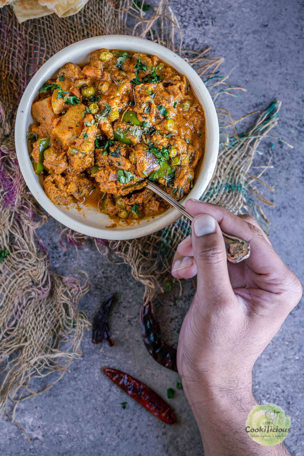 a hand with a spoon in hand digging into a bowl of veg Kolhapuri