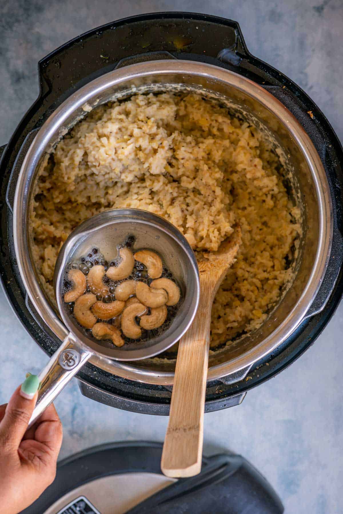 Golden fried cashews and peppercorn tempering being added to Instant Pot Ven Pongal.