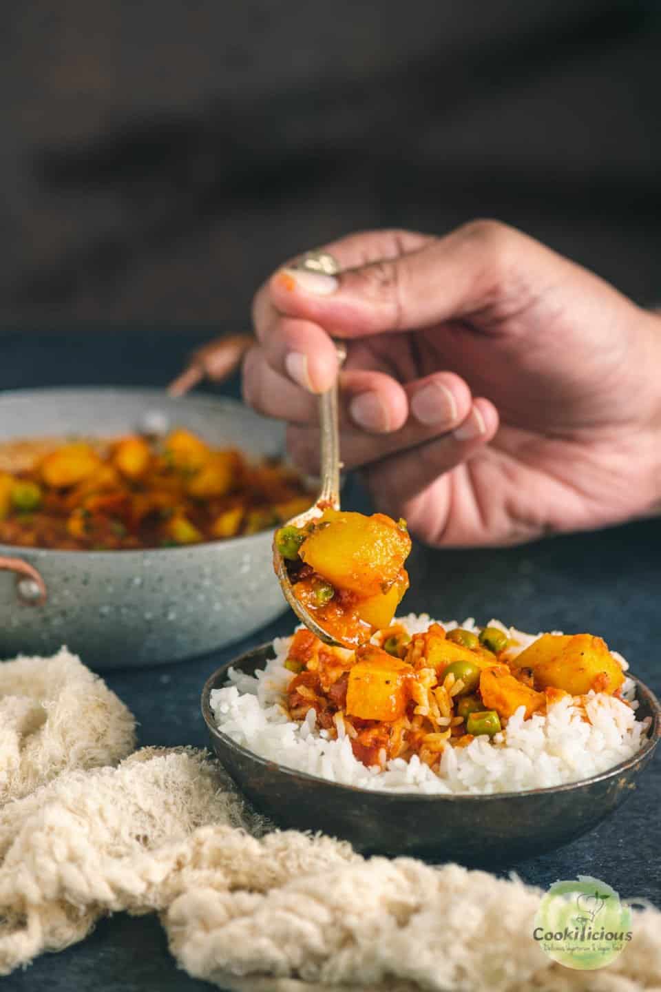 a hand holding a spoon and digging into a bowl of Aloo Matar and rice