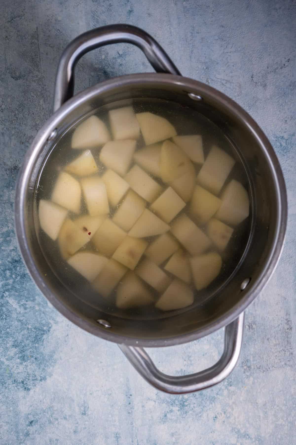 Potatoes and raw plantain boiling in a pot of water for avial recipe.