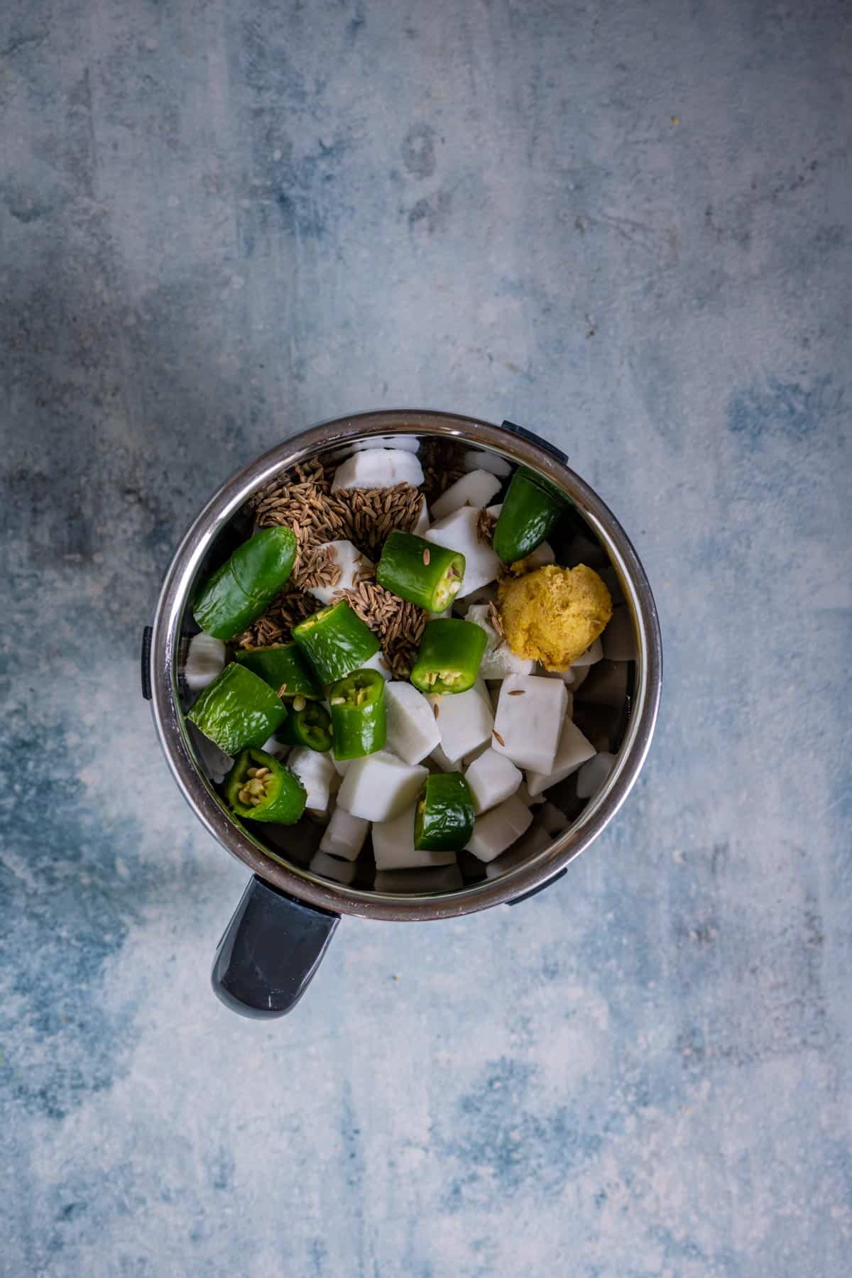 Fresh coconut, cumin seeds, ginger, and green chillies in a blender jar for avial paste.