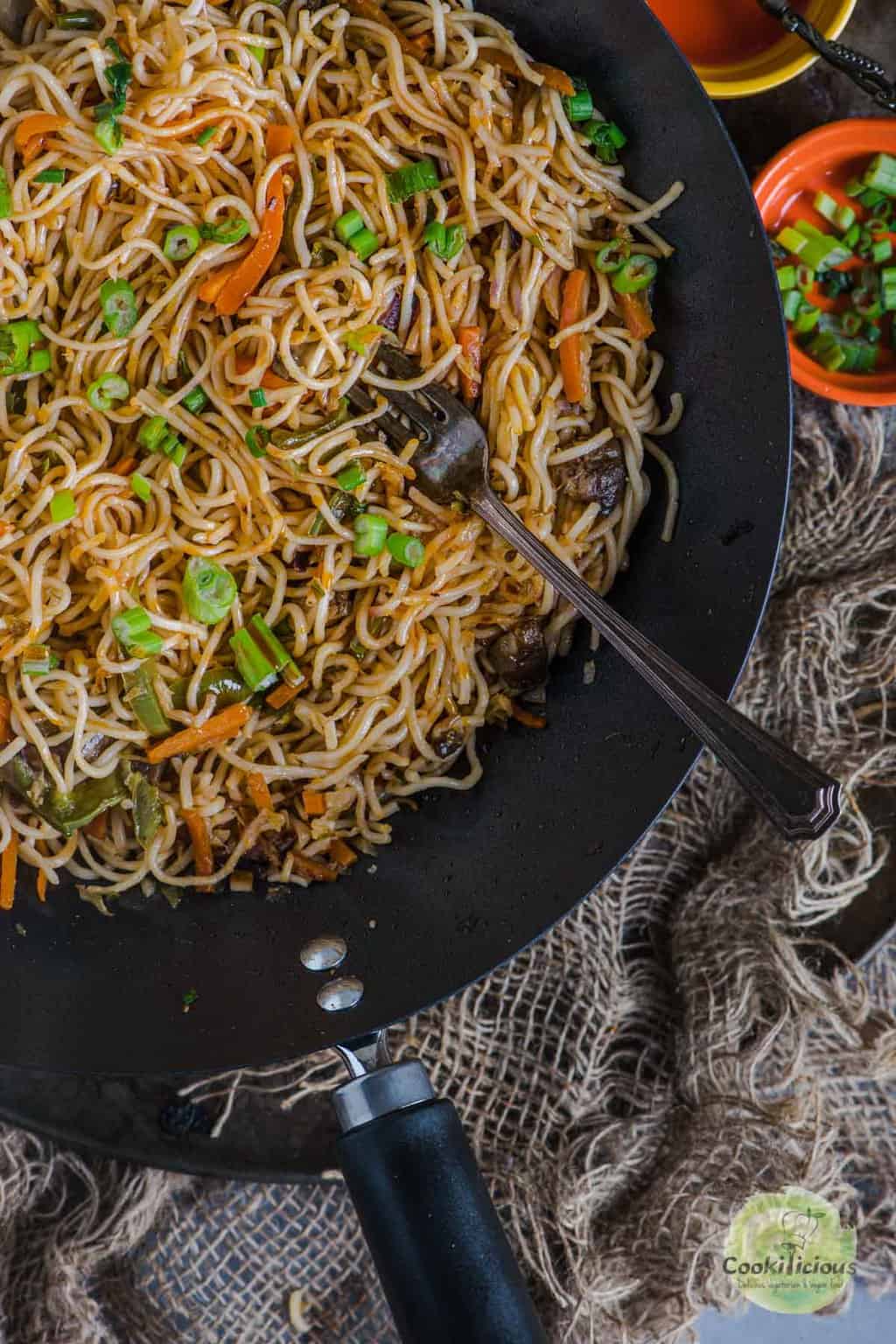 one forth view of a wok with Veg Hakka Noodles and a fork in it