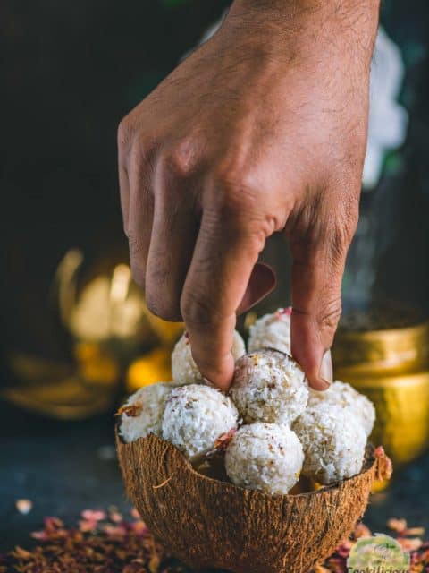 a hand picking up one coconut ladoo from a bowl
