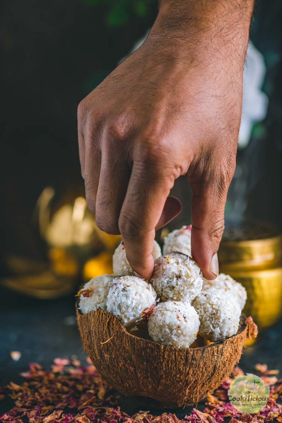 a hand picking up one coconut ladoo from a bowl