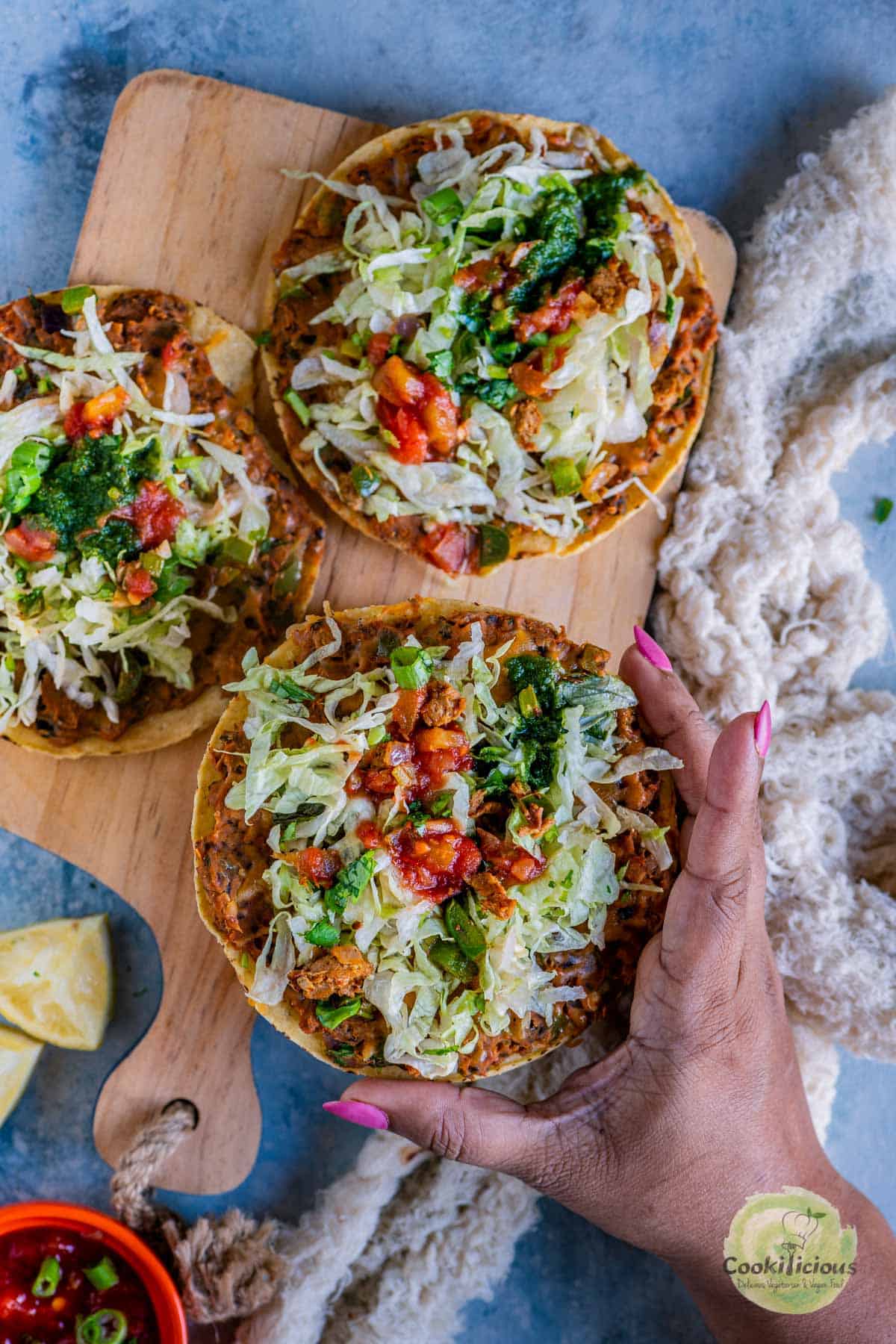 one hand picking up one Vegan Corn Tostada from a wooden platter