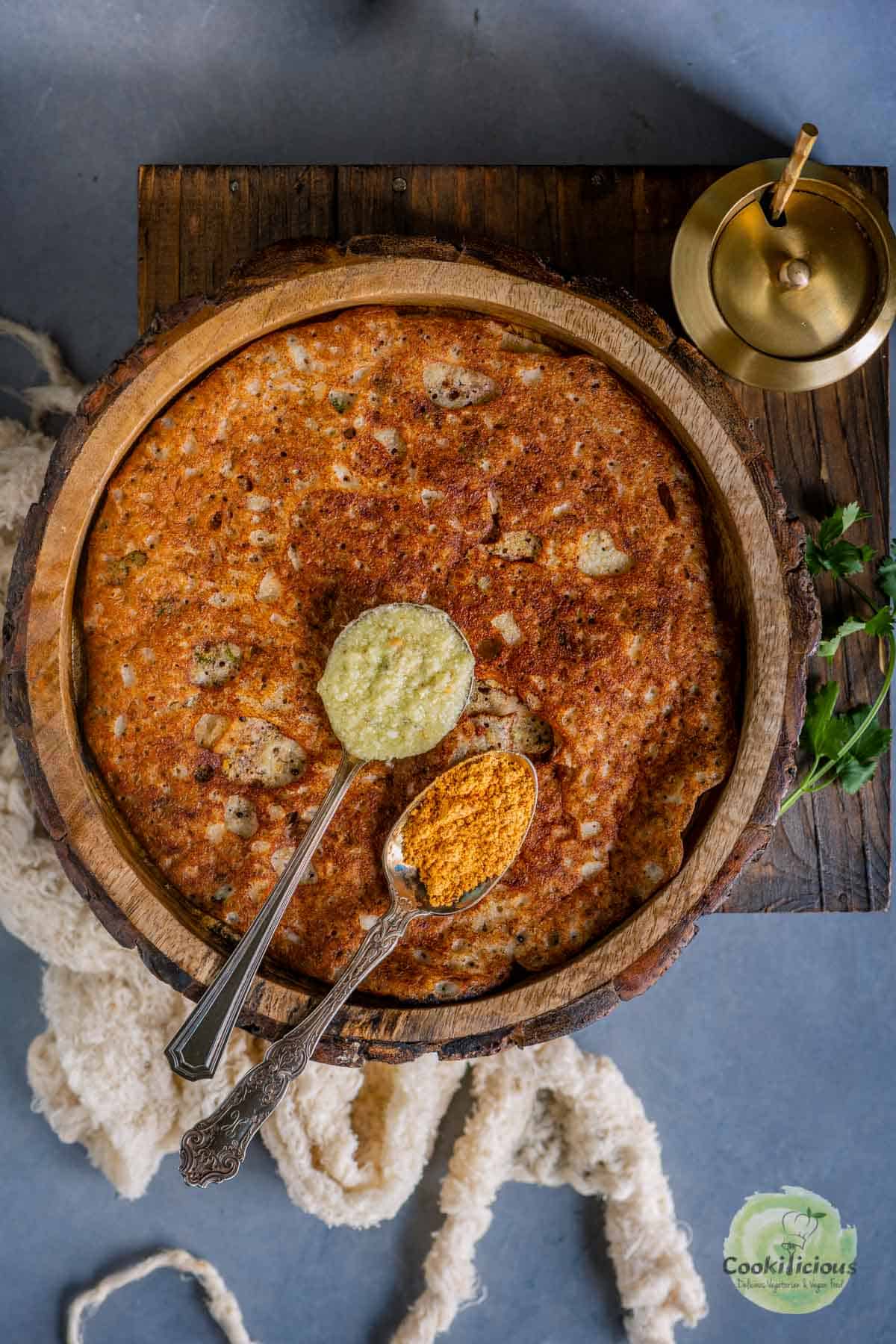 Onion Rava Dosa served in a plate with 2 spoons of chutney over it