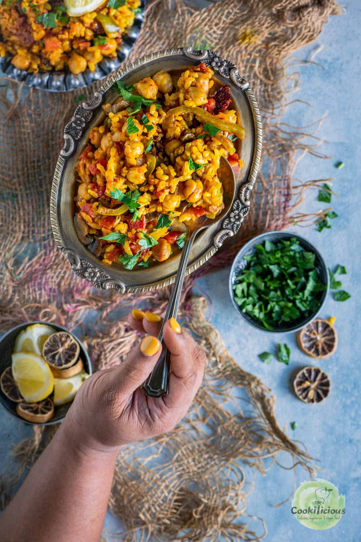 a hand digging into a plate full of Vegan Paella with a spoon