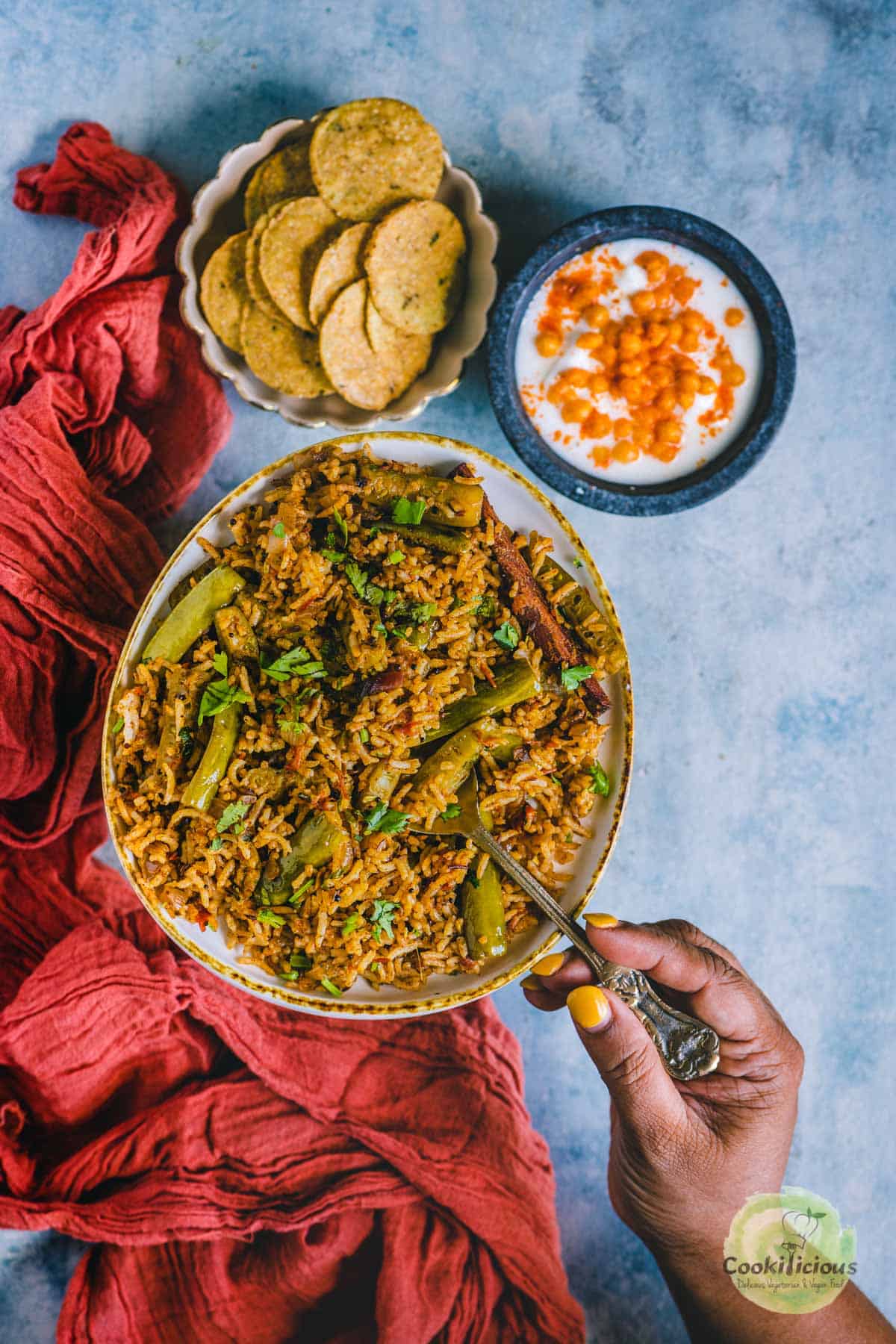 a hand digging into a plate of Tendli Masala Bhaat holding a spoon