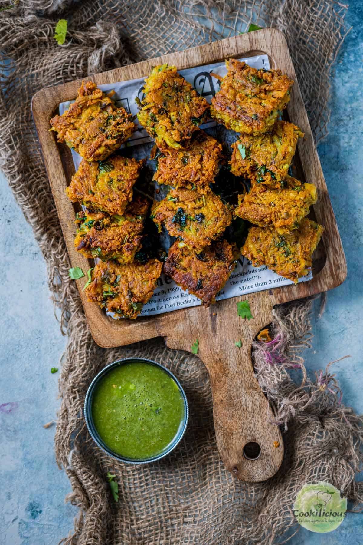 Fried Besan Potato Squares arranged in a wooden platter with green chutney on the side
