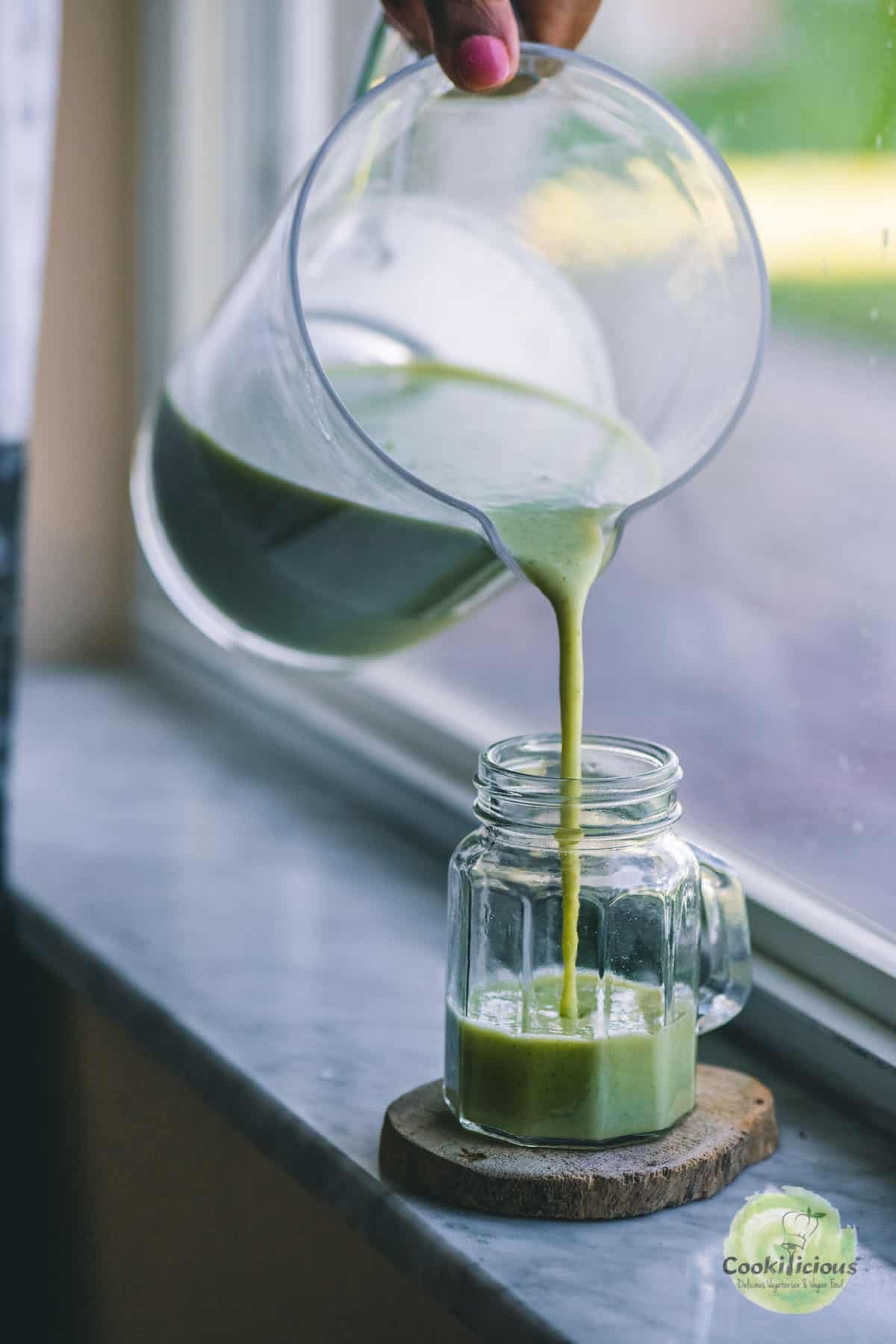 a hand pouring cucumber gazpacho from a blender into a glass